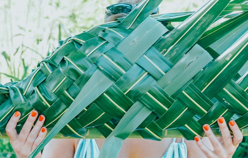 Woman holding up hand woven basket in front of her face to show her handy work at Tropica Island Resort Zero-Carbon Activities